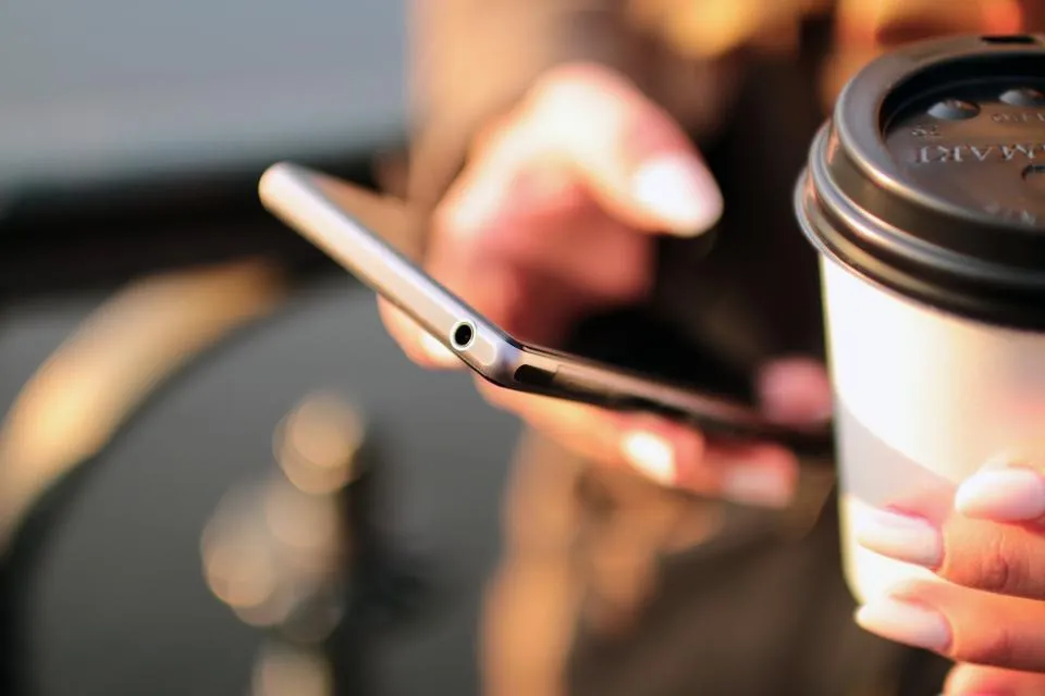 Hand holding a smartphone beside a takeaway coffee cup